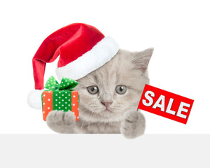 Cute tiny kitten wearing santa hat holding gift box and showing signboard with labeled "sale" above blank white banner. isolated on white background