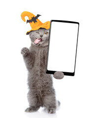 Winking cat with tongue out wearing hat for halloween holds and shows smartphone with white blank screen in it paw. Isolated on white background. Empty space for text