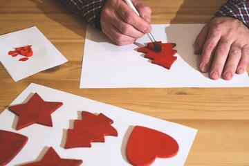 Hands painting a red christmas tree decoration on a wooden table