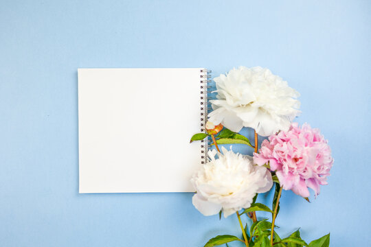 spiral journal next to peonies on table, flatlay of planner and flowers for event organization, open notebook featuring floral sketches and planning details for wedding arrangements