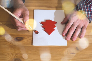 Man painting red wooden christmas tree decorations on paper
