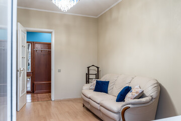 a living room with an outdated design. A large leather sofa, a large wooden wardrobe, and a blue glass chandelier on the ceiling.