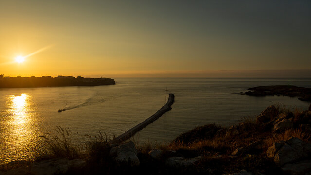 Golden hour sunset over breakwater and fishing boat in Suances, Spain