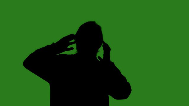 A black isolated silhouette of a woman dancing with her arms raised against a green chroma key background, side view. Minimalistic contrast and modern visual composition, mockup. - Powered by Adobe