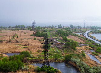 Heavy rain over the lake and the road behind the power line in the field