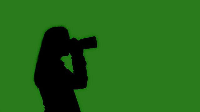 Black isolated silhouette of a woman with a camera on a green chroma key background. Minimalist contrast and modern visual composition, mockup.