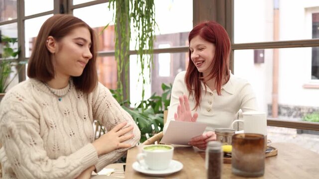 Two friends in a cozy cafe talking one girl admits she has no money while the other smiles and insists on paying supportive moment showing care trust understanding in a relaxed atmosphere