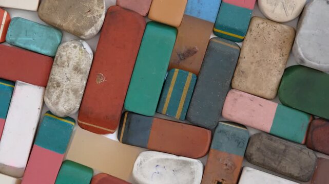 A collection of various used and worn-out erasers, flat lay photograph of a scattered collection of vintage, heavily used, and well-worn rectangular erasers