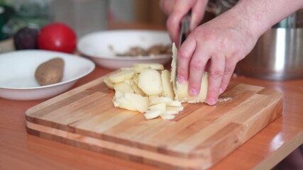 Male hands dicing a peeled, boiled potato on a wooden cutting board in a kitchen