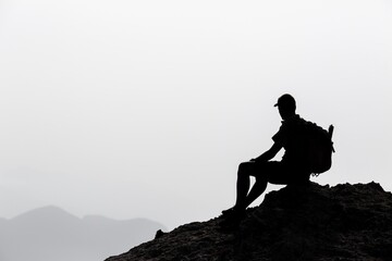 Silhouette of a hiker sitting on a mountain peak observing the view