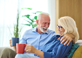 Portrait of a happy senior couple embracing talking and drinking coffee or tea at home