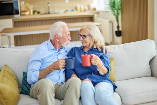 Portrait of a happy senior couple embracing talking and drinking coffee or tea at home - Powered by Adobe