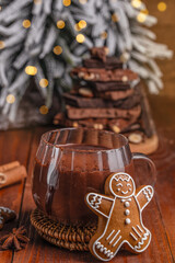 Cup of rich hot chocolate with gingerbread cookie on wooden table in cozy Christmas setting, festive background with bokeh lights, cinnamon sticks and chocolate pieces, winter holiday mood