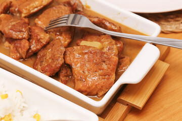 Roasted pork neck in brown sauce served on white dish. Homemade dinner concept with baked meat, rich gravy, and fork on wooden table. Tasty traditional meal closeup.