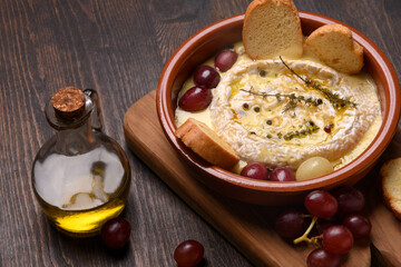 Baked brie cheese with honey, grapes, aromatic herbs and crusty bread, baked camembert	