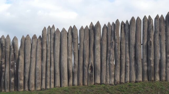 Old wooden fence from sharp logs against the sky.