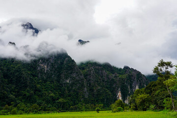 Fog rolling over dramatic karst mountains above lush green fields, Vang Vieng, Laos