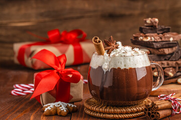 Cup of hot chocolate with whipped cream, cinnamon stick and star anise on rustic wooden table, Christmas composition with gifts and chocolate pieces, cozy festive atmosphere for winter holiday design