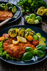 Crispy breaded chicken cutlet with boiled potatoes and Brussels sprouts on wooden table