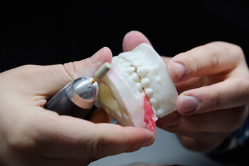 Dental technician using a drill to adjust and polish a large jaw model.