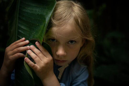 Preschool girl hiding behind palm leaf.