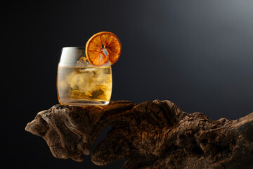 Old fashioned cocktail with ice and dried orange slice on a old snag.