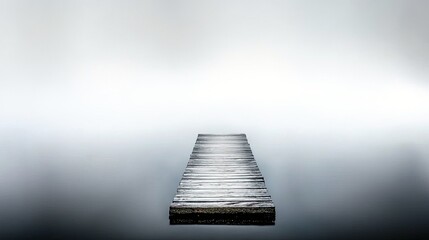A wooden pier juts out into a vast expanse of still, misty water, creating a serene and minimalist landscape.