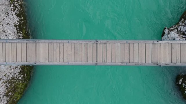 Top down aerial view of a wooden suspension bridge crossing the beautiful emerald Soca River in Slovenia