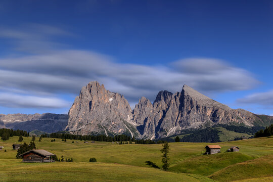 View over the alpine meadows with mountain cabins towards the Langkofel group with the peaks of Langkofel and Plattkofel on the Seiser Alm, Dolomites, South Tyrol, Italy. - Powered by Adobe