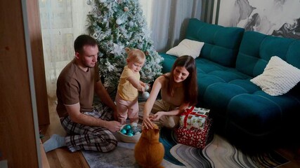 festive family celebration, warm family gathering around decorated christmas tree, happy family unwrapping presents beneath brightly decorated tree with curious ginger