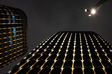 A dramatic worm's-eye view of modern skyscrapers. Their illuminated facades create a powerful pattern of light against the dark night sky, symbolizing ambition and success.