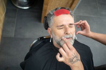 Man receiving professional eyebrow grooming at barber salon, close-up personal care.
