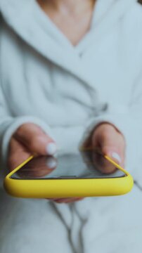 Using a smartphClose-up of a person's hands using a phone, holding a smartphone and browsing social media. The screen glows softly, reflecting off the user's fingersone to scroll through social media 