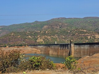 Mountain dam landscape Wide view of a dam surrounded by green hills and dry vegetation under bright sunlight, capturing natural engineering amidst rugged terrain.