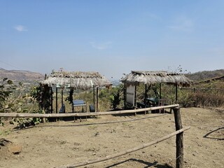 Countryside shelter A handmade straw-roof hut beside a dirt road, set against a scenic mountain backdrop and open horizon, ideal for nature or travel themes.