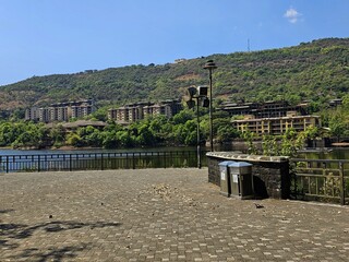 Lakeside promenade view Stone-paved lakeside walkway with railings and scenic hilltop buildings in the background under clear blue skies, perfect for travel and architecture themes.