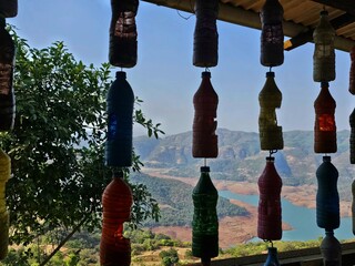 Hanging bottle art Row of colorful recycled plastic bottles hanging as decor with stunning valley and lake view in the background, representing creativity and sustainability.