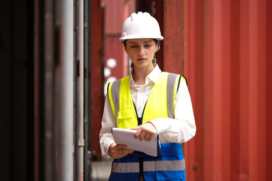 Industrial engineer standing at shipping container yard inspecting cargo delivering loading plan. Female logistic manager using laptop examining import export schedule for international distribution