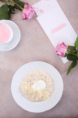Oatmeal porridge with poached egg and parmesan cheese. Bouquet of pink roses on the table. Healthy eating. Concept of breakfast. Flat lay. Top view. Copy space.