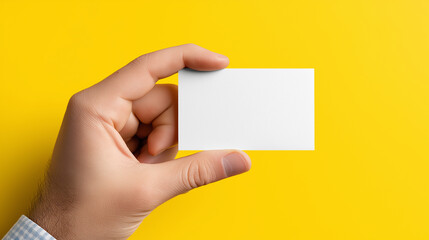 Hand holding blank white business card against bright yellow background for showcasing minimalist design.