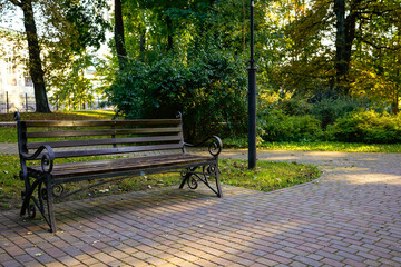 ornate bench under canopy of trees, weathered wood and iron detailing beside brick walkway with dappled afternoon light, inviting quiet reading or restful pause in leafy neighborhood