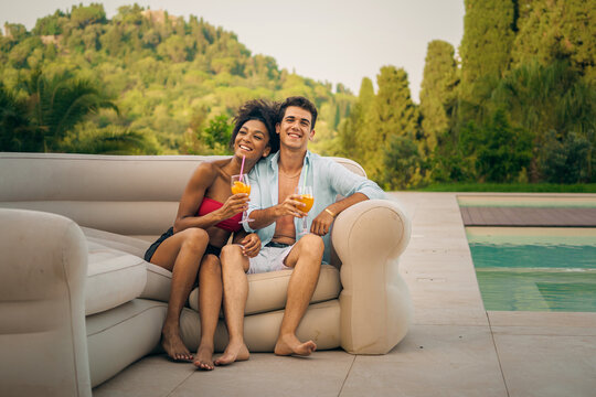 Happy couple enjoying refreshing drinks by the poolside in a sunny garden setting, capturing a joyful moment - Powered by Adobe