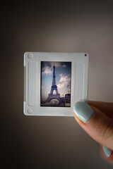 Woman's hand holding a retro slide transparency displaying a classic view of the Eiffel Tower under a cloudy sky, evoking travel memories and nostalgia