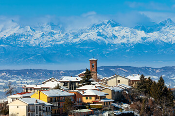 Italian village with colorful houses and a historic bell tower as snow-covered mountains and under clear blue sky on background.