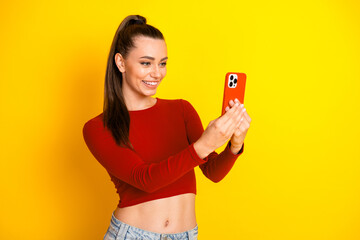 Smiling young woman selfie in red cropped top against bright yellow background, showcasing casual fashion and confident lifestyle