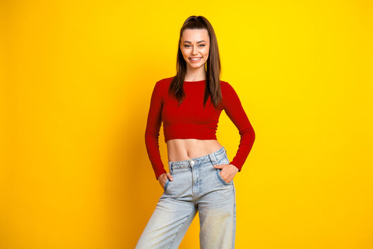 Fototapeta Young brunette woman in red crop top and jeans stands against a yellow background smiling confidently for lifestyle fashion promotion