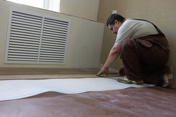 A man lays laminate flooring throughout his home. A man in work overalls lays insulation and joins...