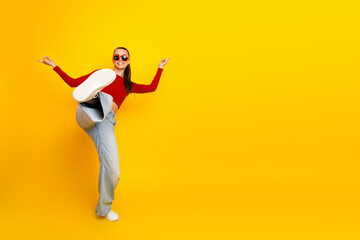 Young woman in red top and jeans dancing against bright yellow background smiling and stylish fashion model lifestyle image