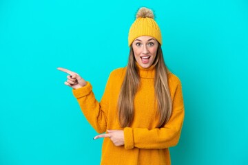 Young caucasian woman wearing winter jacket isolated on blue background surprised and pointing side