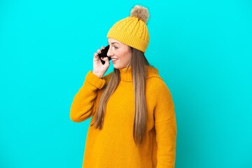 Young caucasian woman wearing winter jacket isolated on blue background keeping a conversation with...